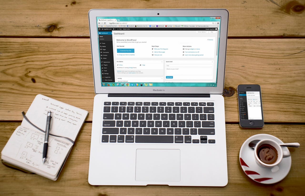 Turned-on Macbook Air Beside Black Iphone 4, Cup of Tea, and Notebook on Brown Wooden Surface